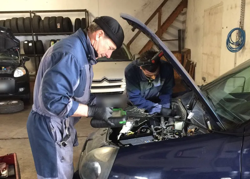 Deux mécaniciens d'AP Auto penchés sur le moteur d'une voiture, capot ouvert